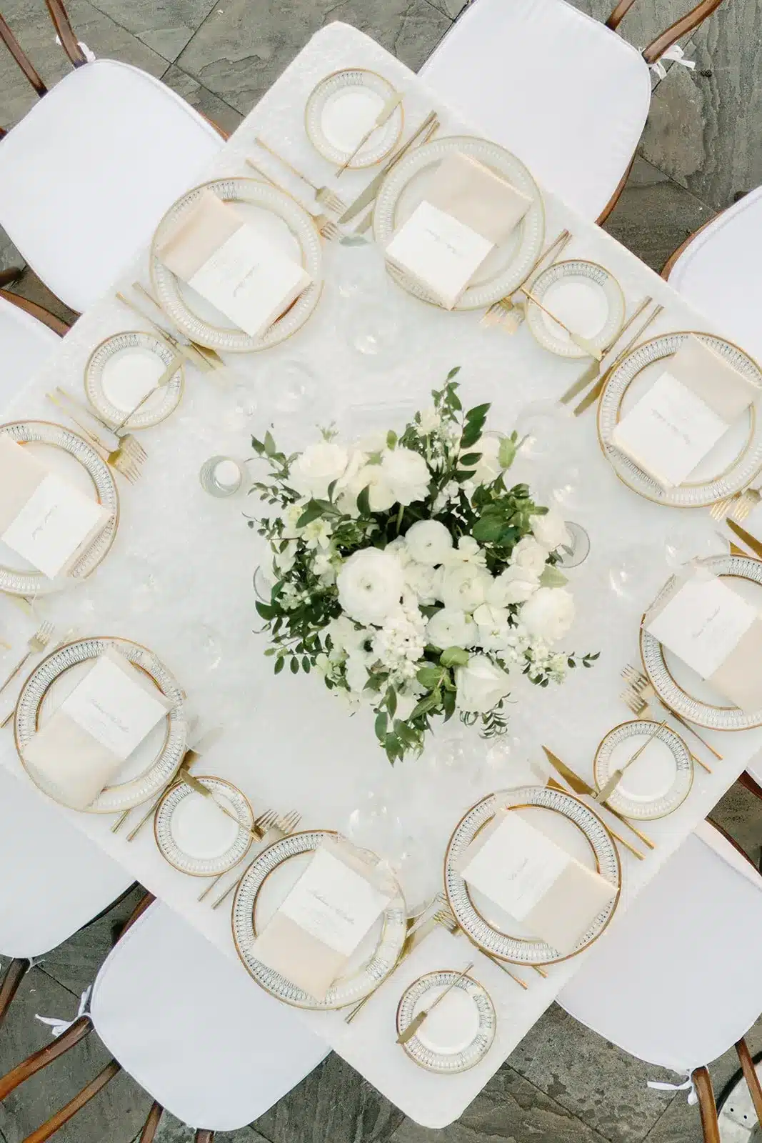 Overhead view of a round wedding table with white florals, gold-rimmed plates, and place cards. | Curated Events Overhead view of a round wedding table with white florals, gold-rimmed plates, and place cards.