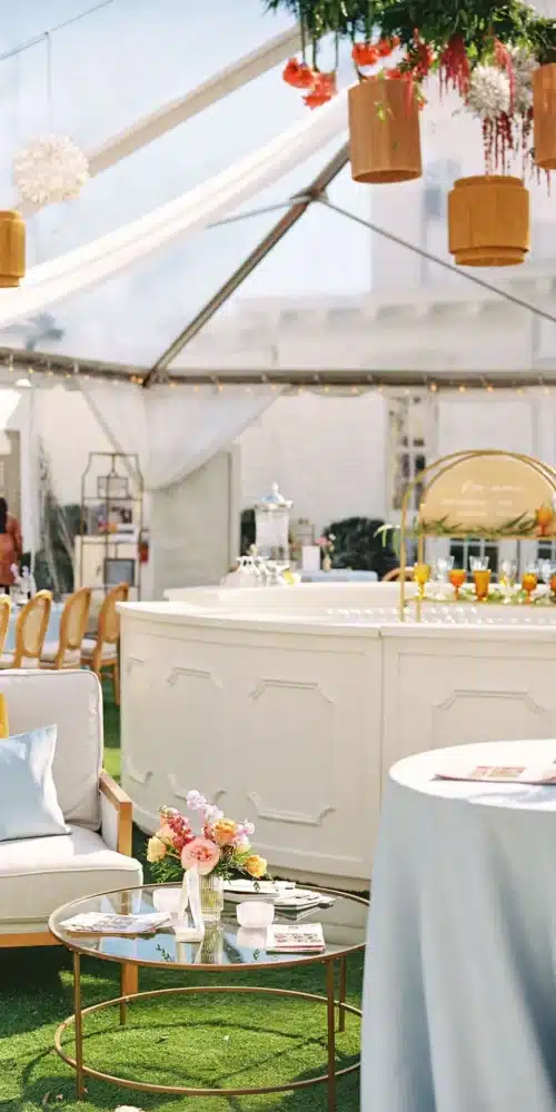 Clear-top backyard tent with round white bar, lounge seating, and hanging wood pendants.