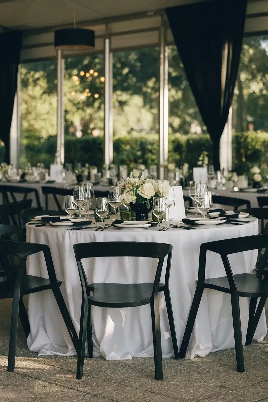 Round reception table with white linens, black chairs, and classic floral centerpiece.