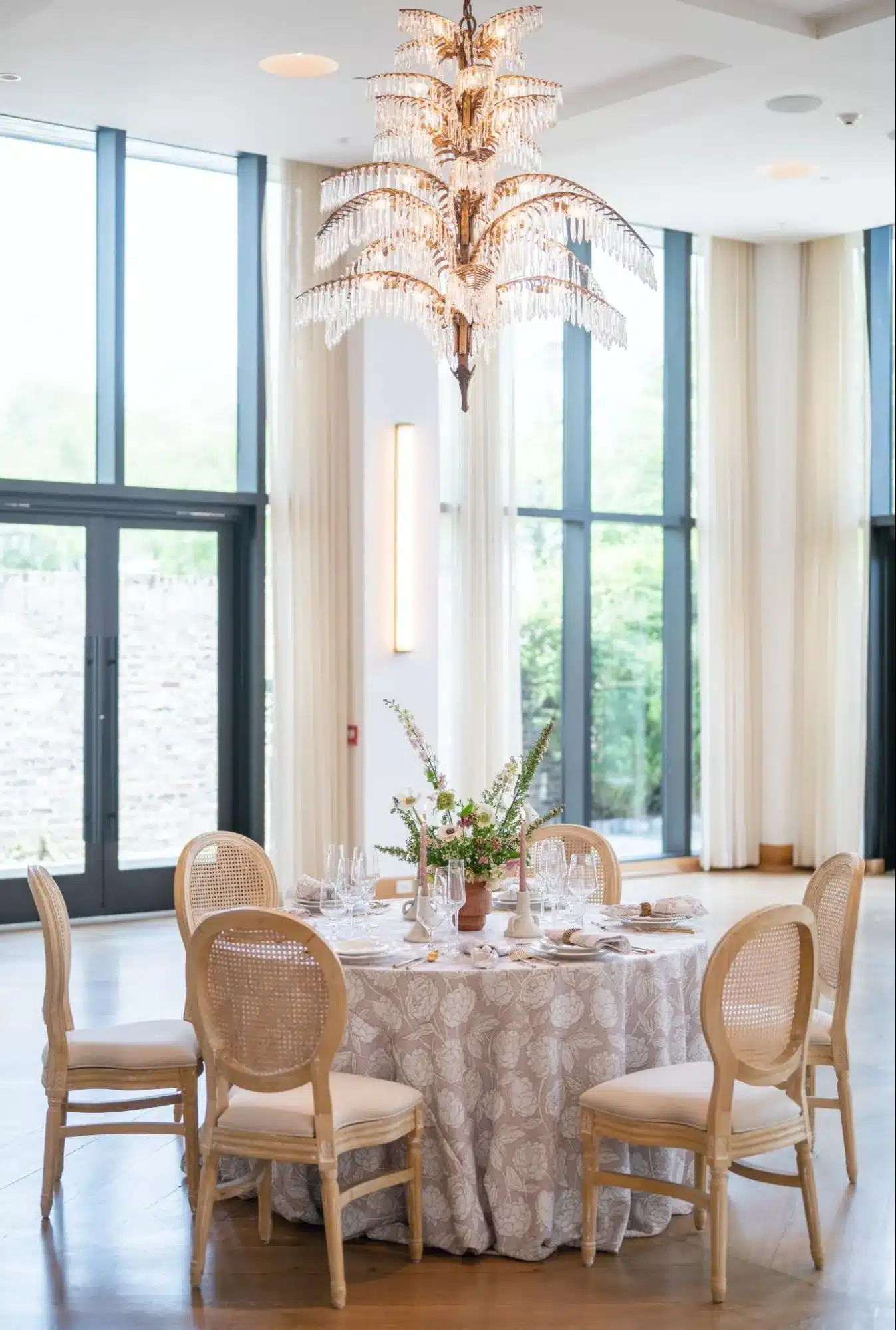 Elegant indoor round table with patterned linen and crystal chandelier overhead.