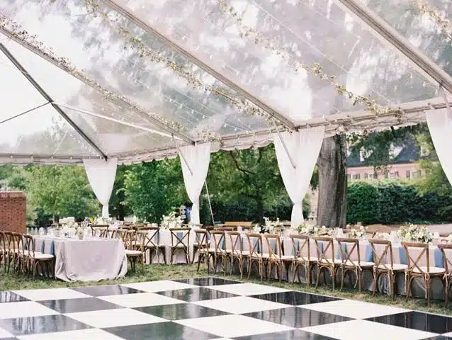 Clear-top tent reception with long banquet tables and a black-and-white checkered dance floor.