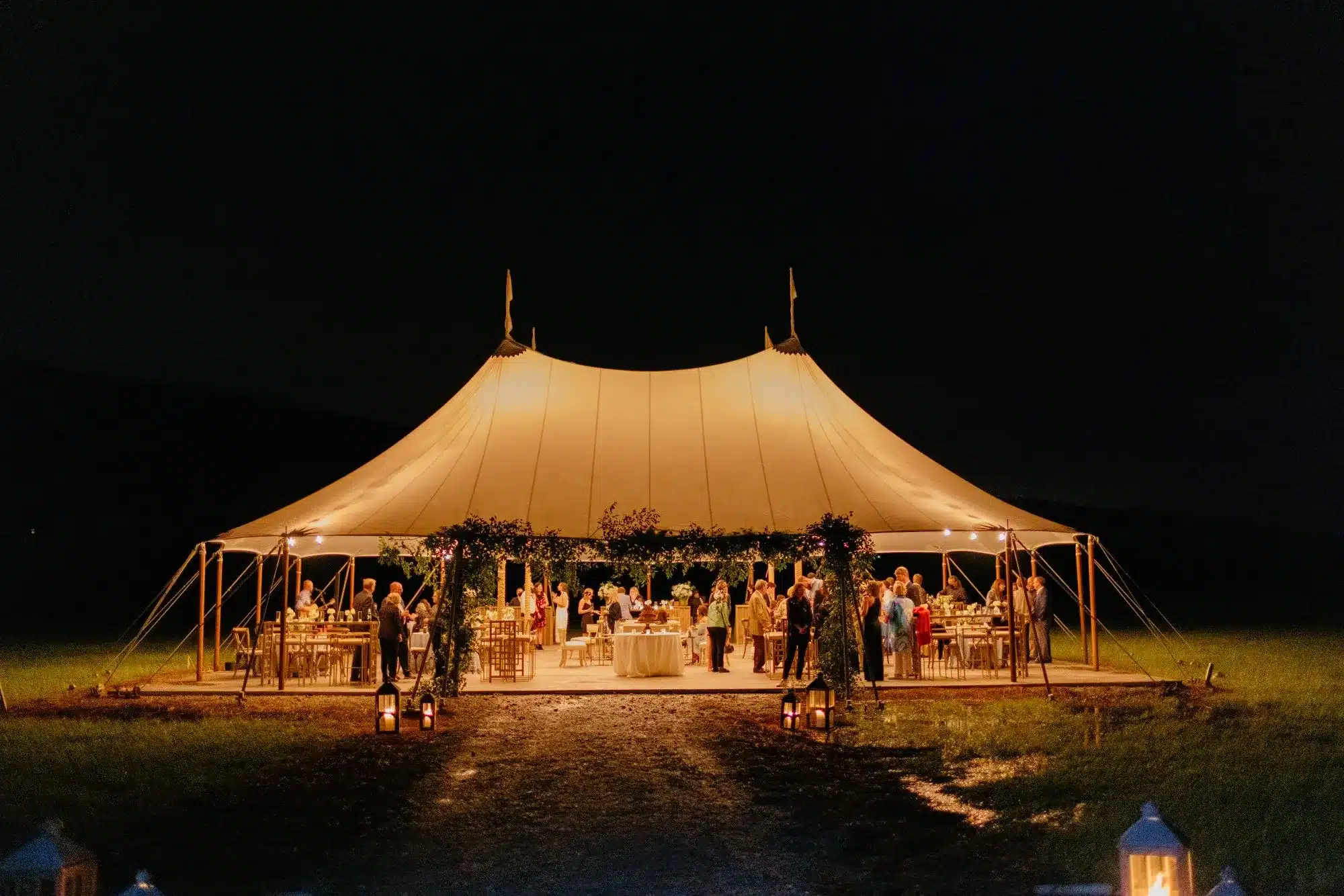 Sailcloth tent glowing at night with guests gathered inside.