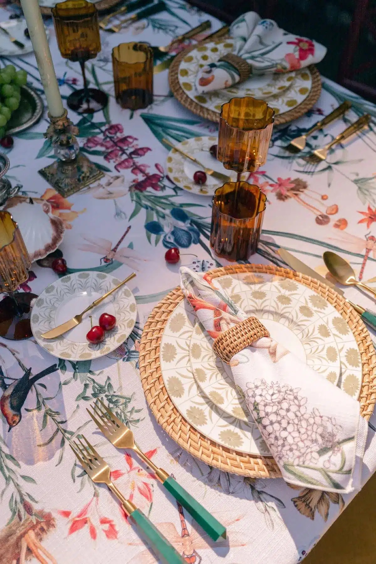 Vibrant botanical table linen styled with woven chargers, amber glassware, and gold flatware for a festive event.