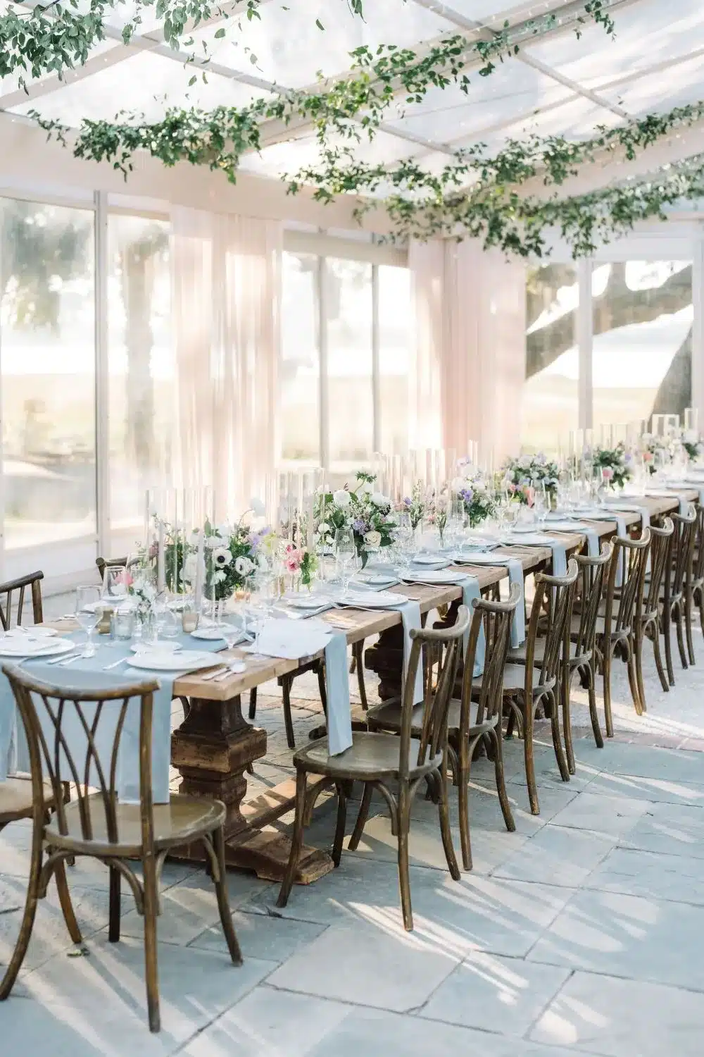 Long reception table with place settings and florals inside a light-filled tented space. | Curated Events Long reception table with place settings and florals inside a light-filled tented space.