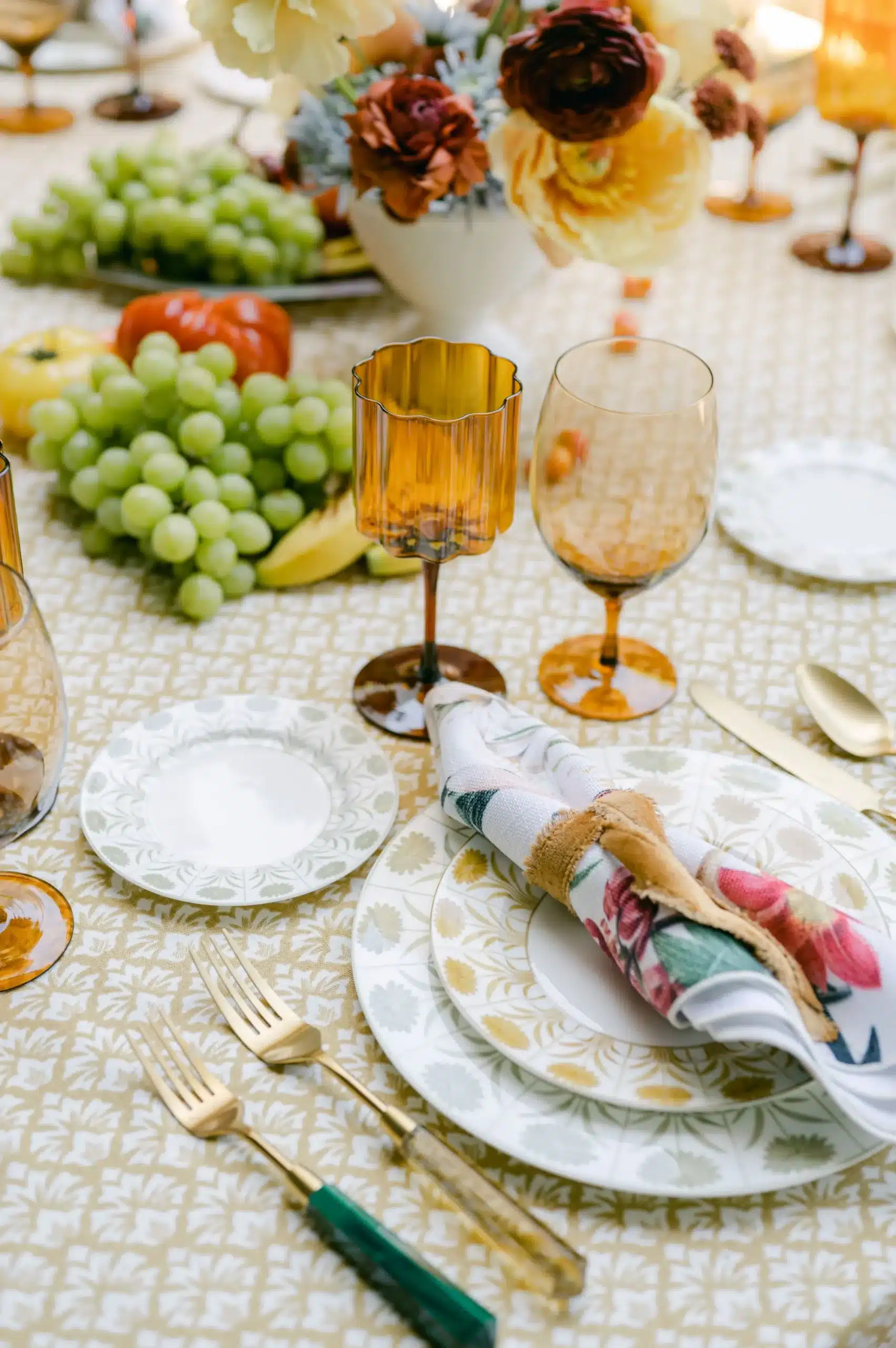 Patterned tablescape with amber glassware, gold flatware, and floral napkin detail.