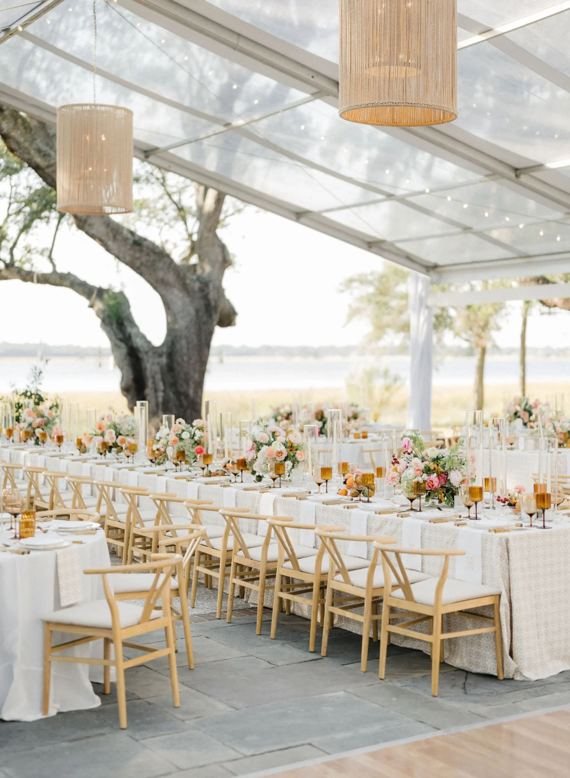 Clear top tent with hanging lanterns over long tables by the water