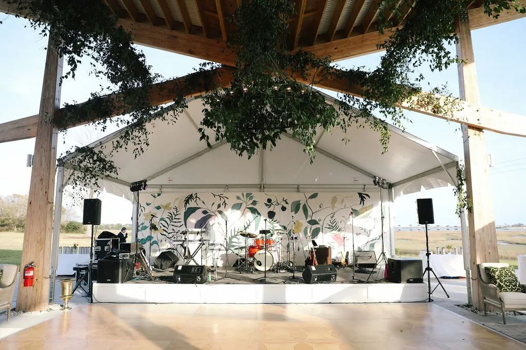 Covered outdoor stage with band setup and greenery for live event entertainment.
