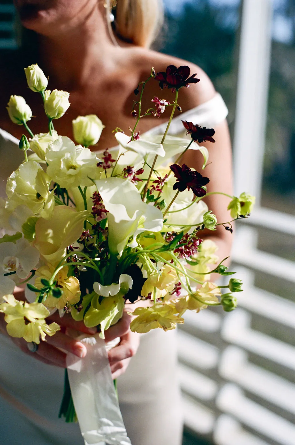 Bride holding bouquet of white and deep burgundy flowers in soft natural light.