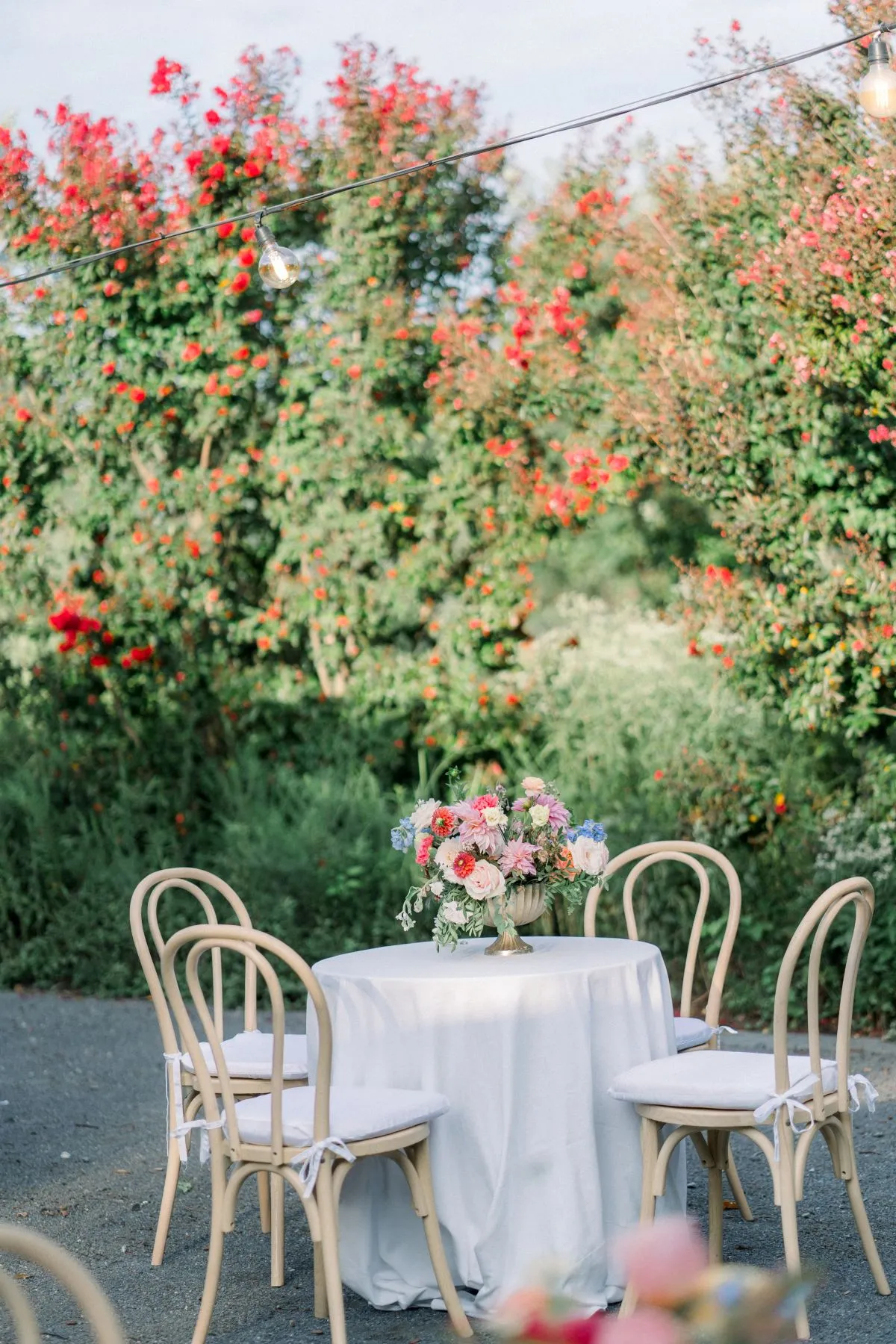 Small round table with pastel floral centerpiece and wooden chairs in garden setting