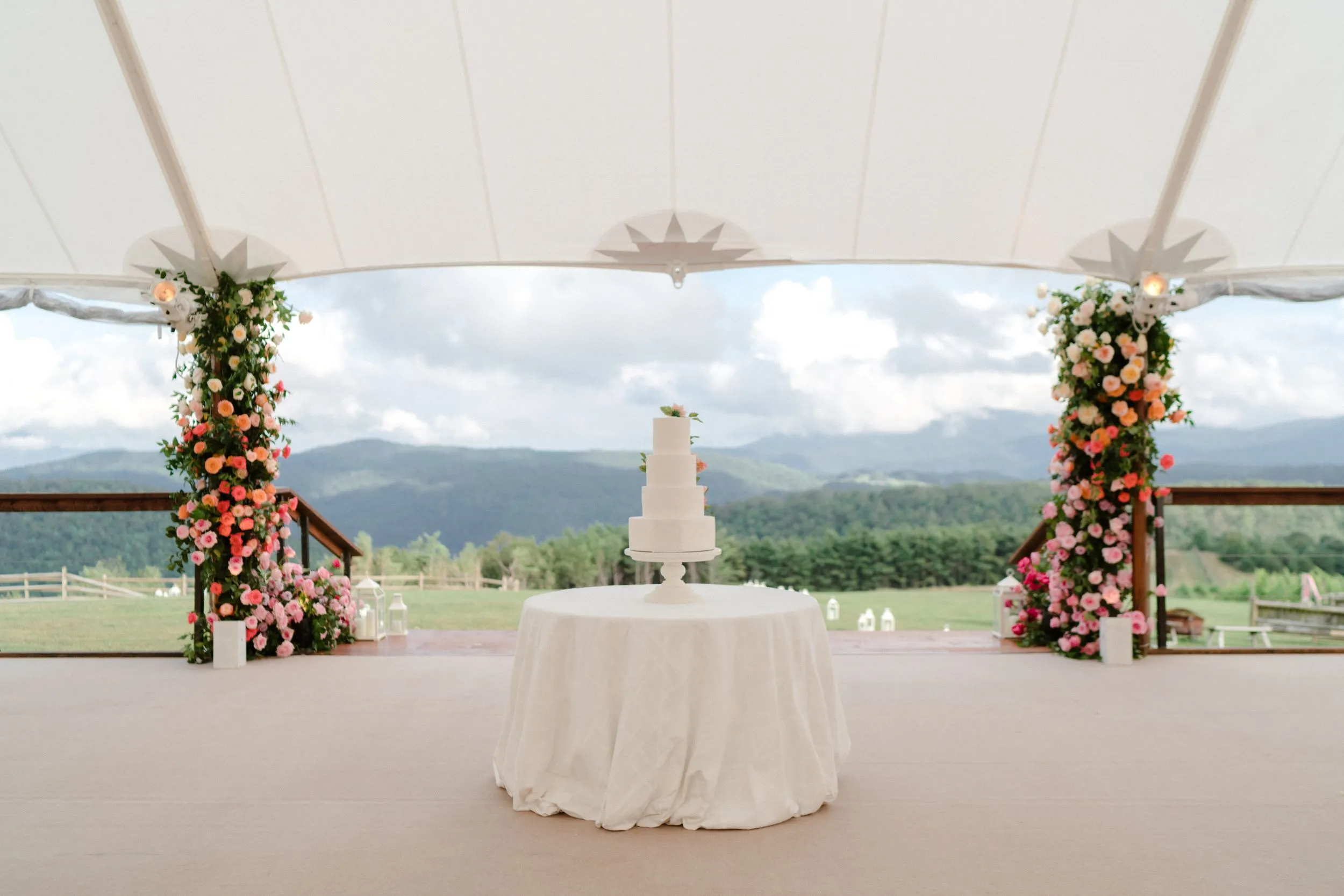 Wedding cake display under tent with floral pillars and mountain backdrop | Curated Events Wedding cake display under tent with floral pillars and mountain backdrop