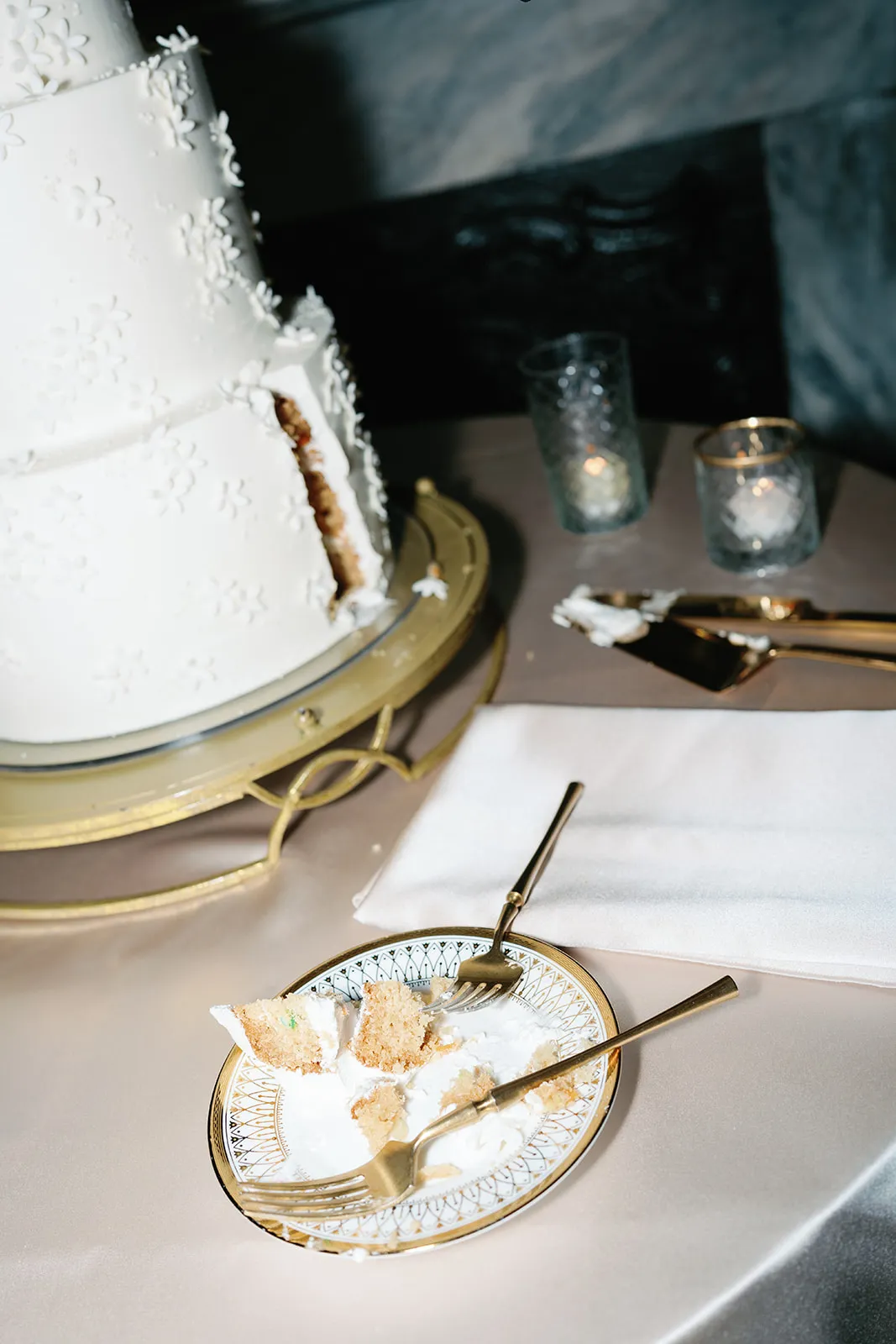 Wedding cake table with partially served cake, gold stand, and dessert place setting