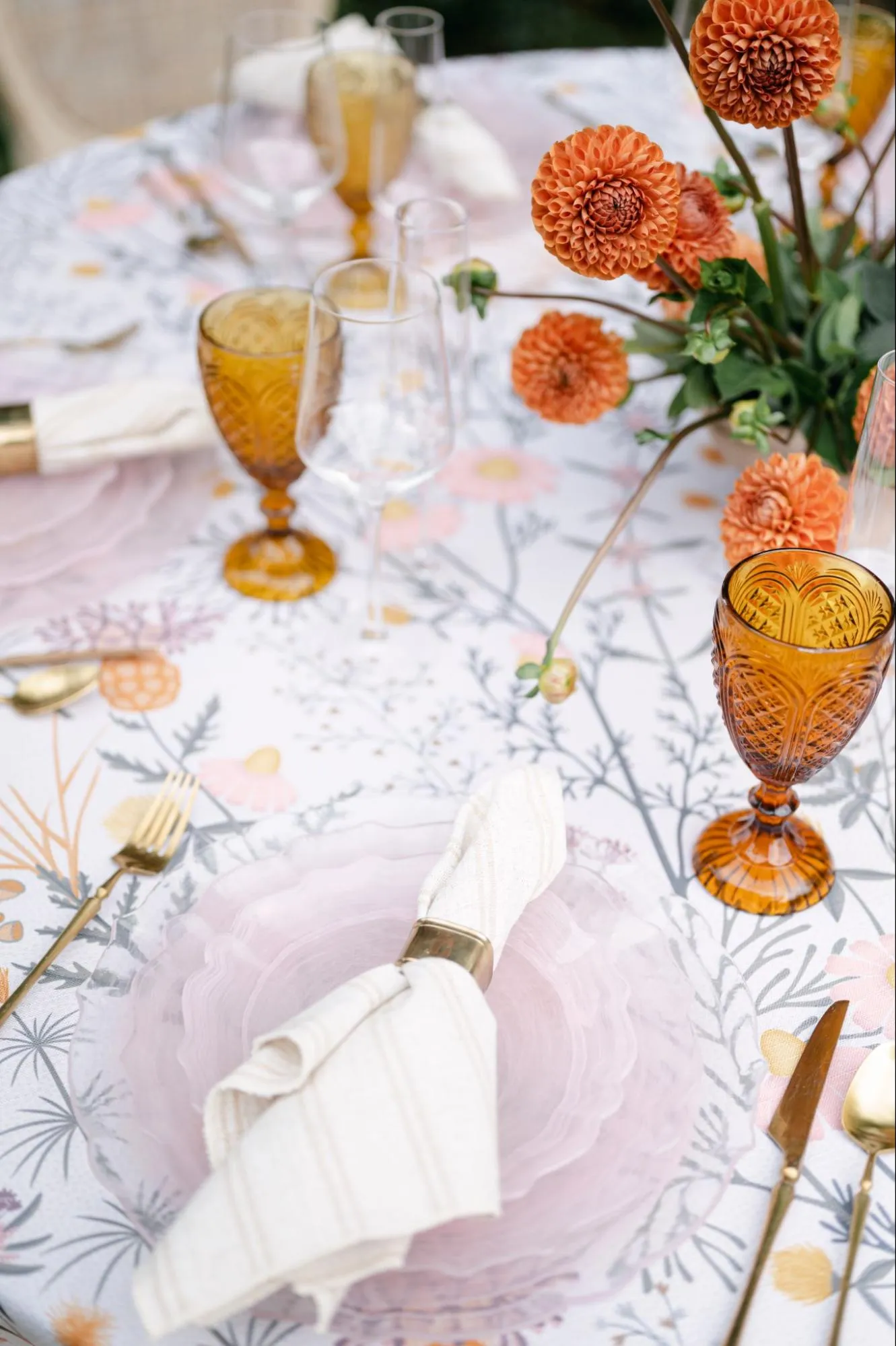 Close-up of patterned table linen with amber glassware and orange floral arrangement