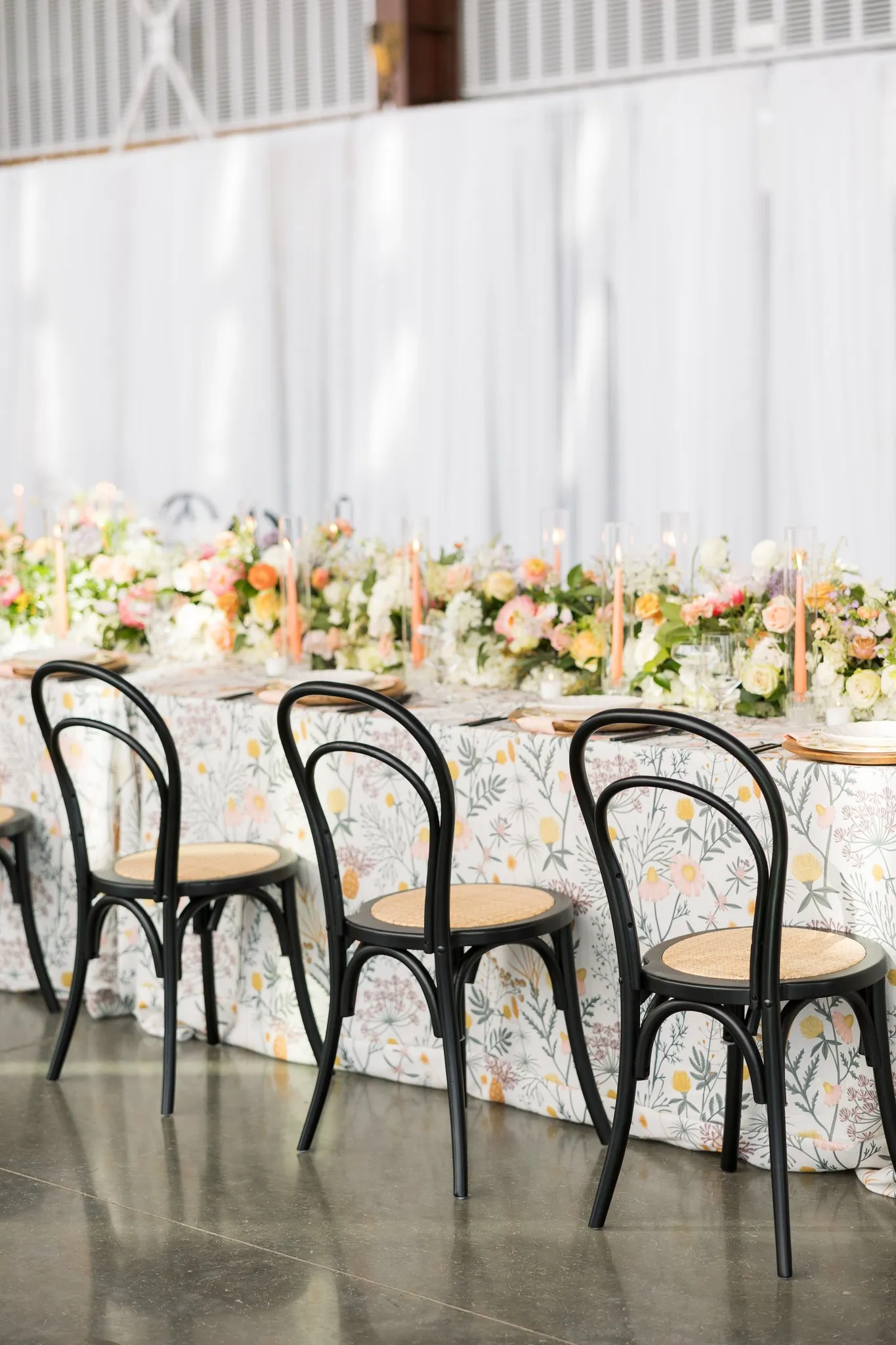 Long banquet table with floral linen, low arrangements, and black bistro chairs
