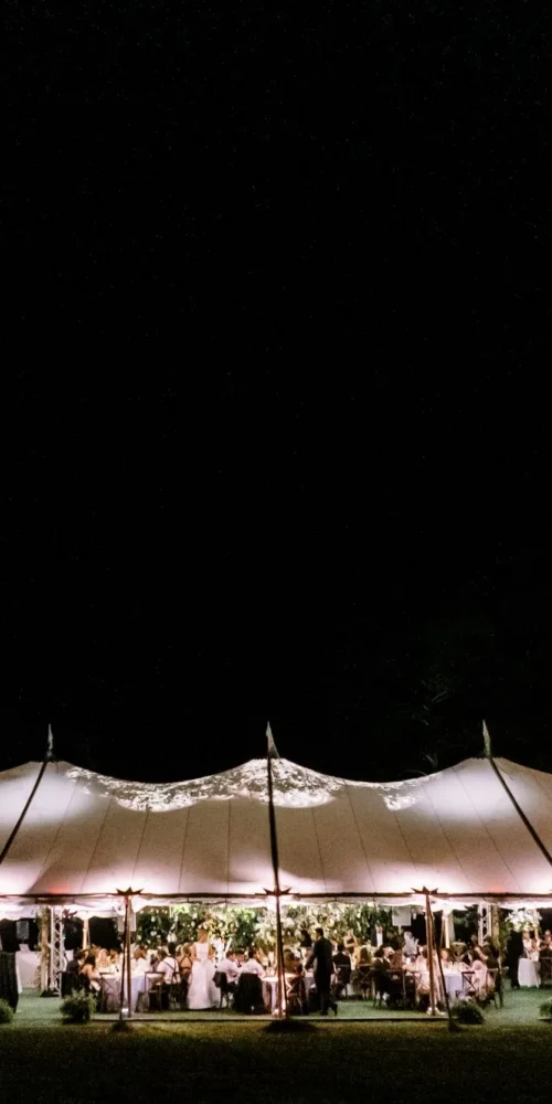 Large outdoor event tent glowing at night with warm ambient lighting and guests inside