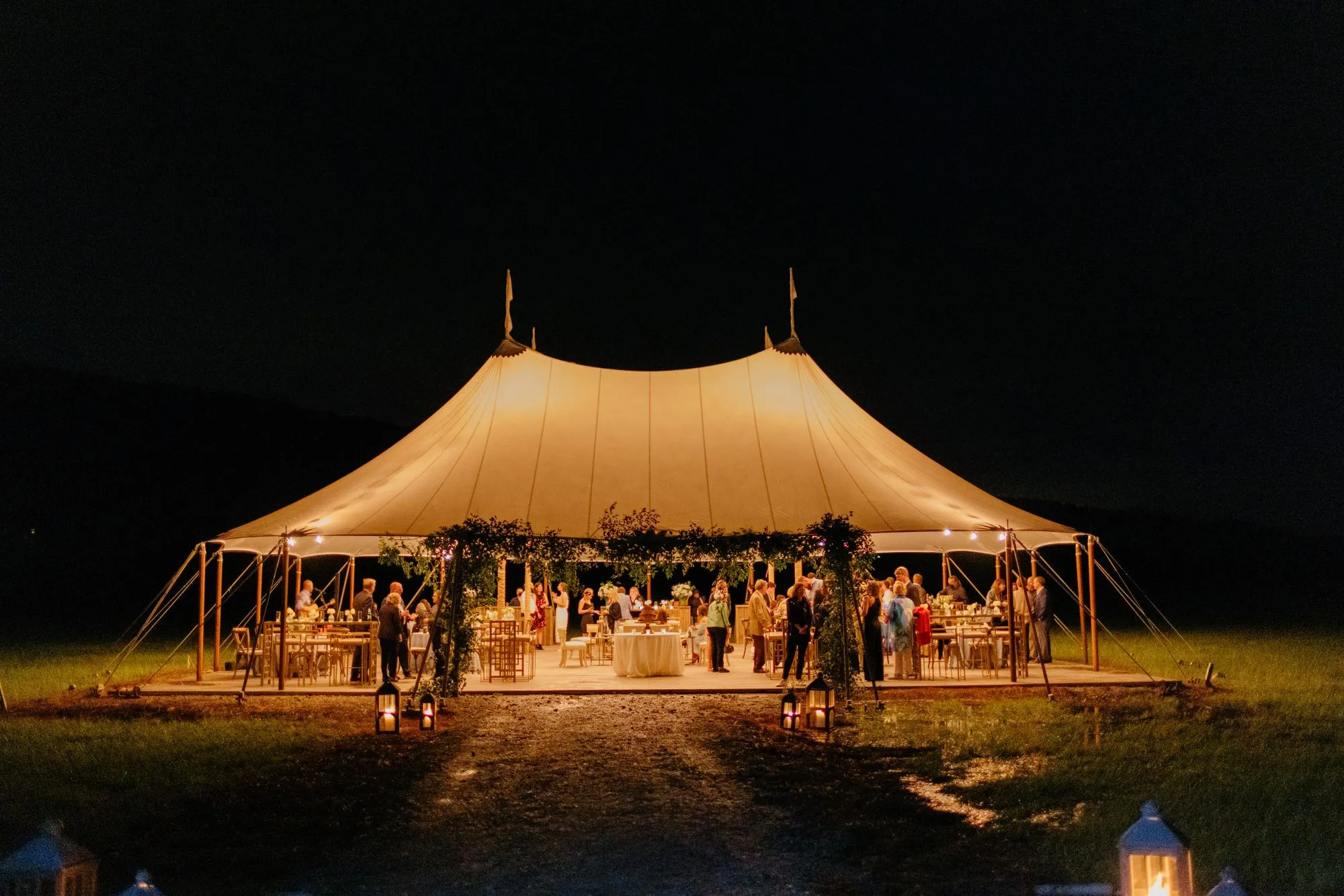 Outdoor wedding tent glowing at night with guests dining under warm lighting