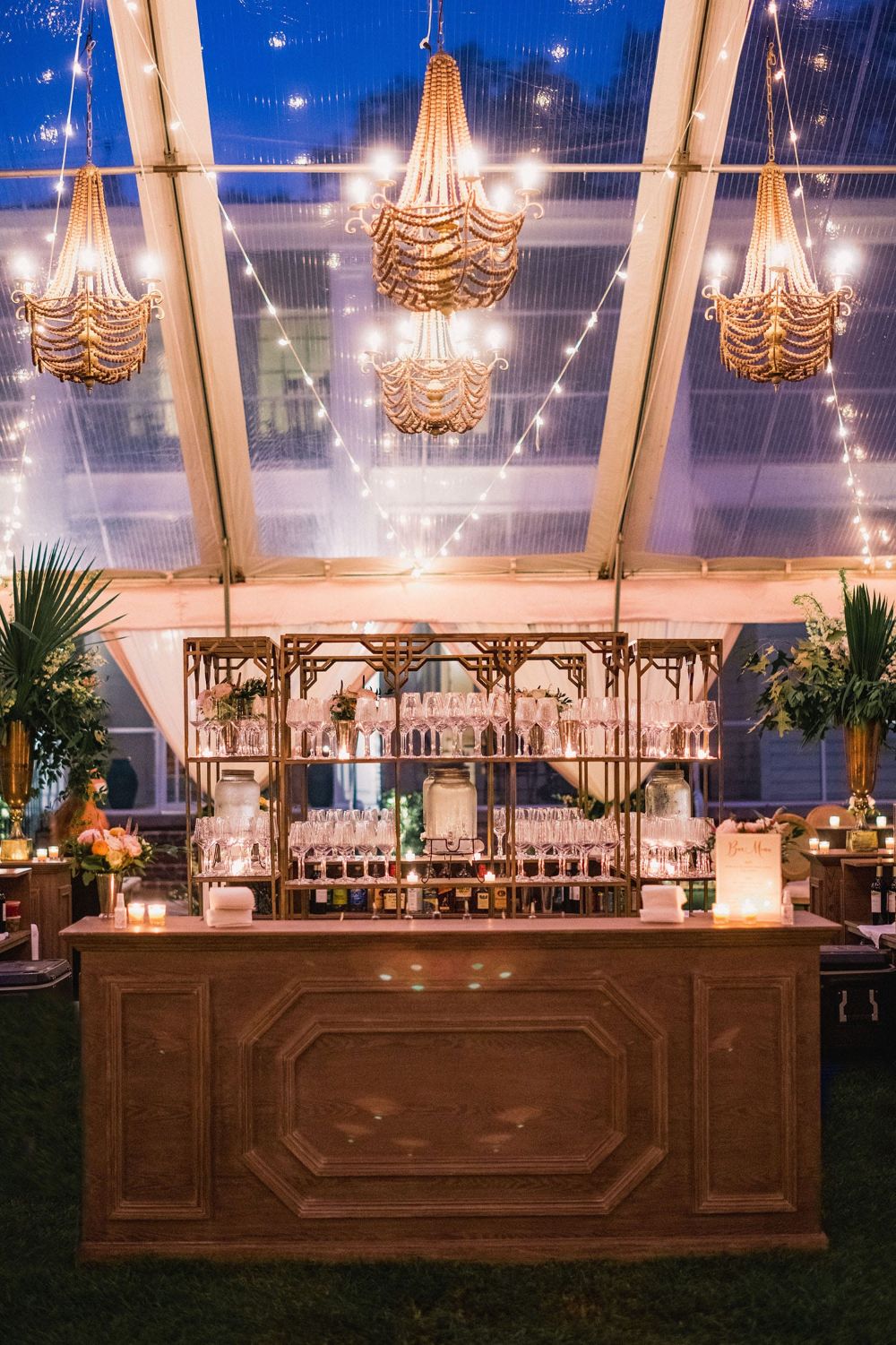 Luxurious bar display inside a clear-top tent with chandeliers, glassware, and warm lighting