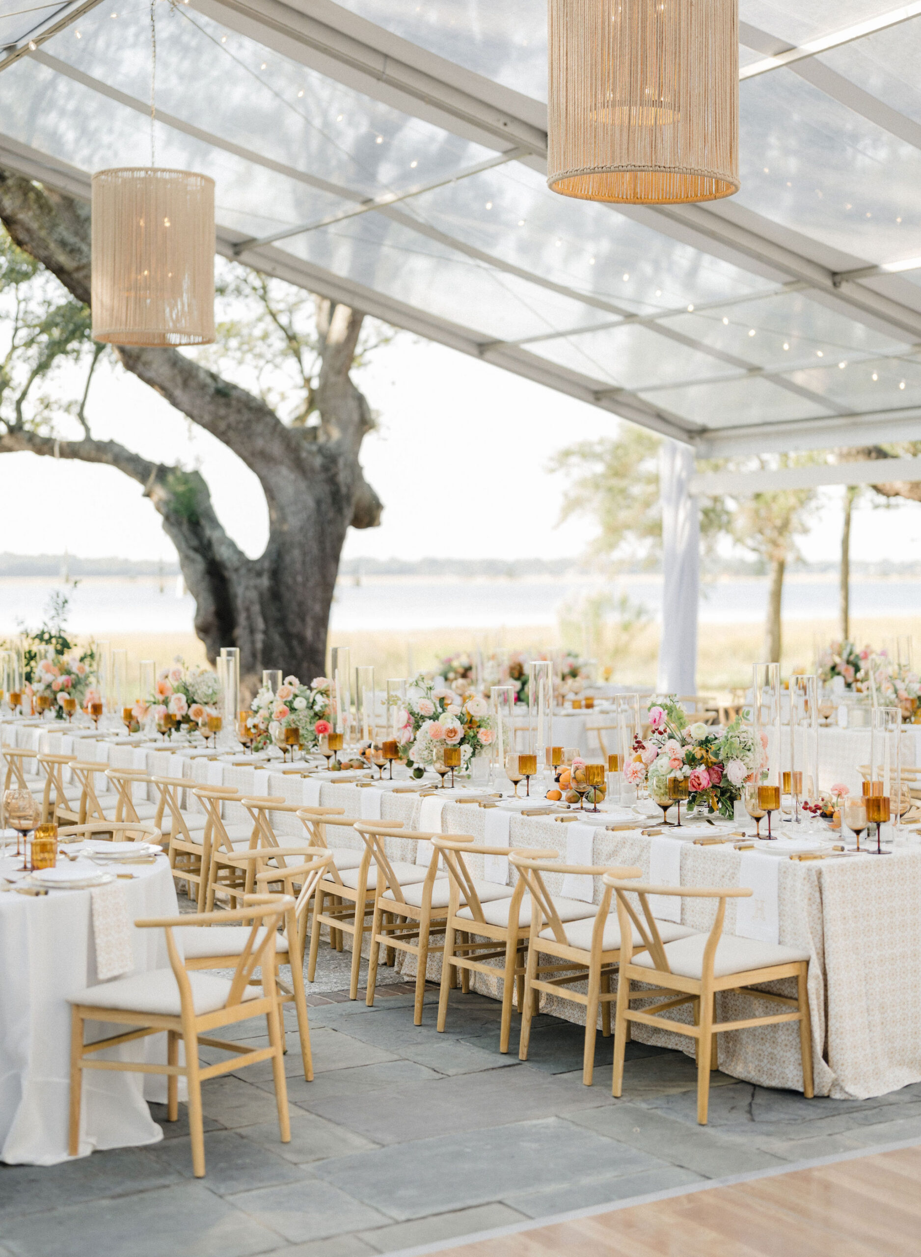Clear-top tent reception with long tables, floral centerpieces, and waterfront views