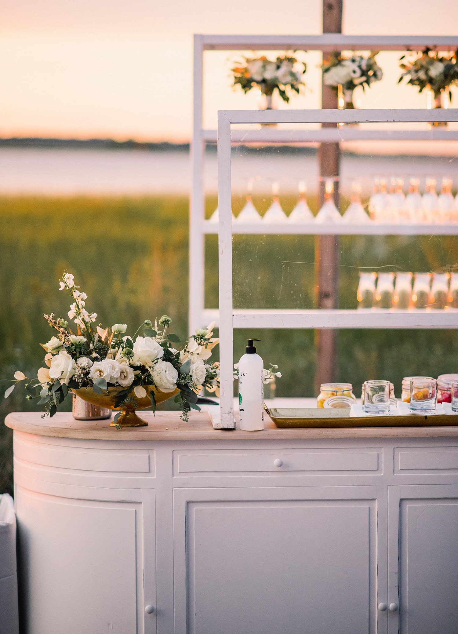 Minimalist bar with white shelving, floral arrangement, and drinks set against a waterfront backdrop