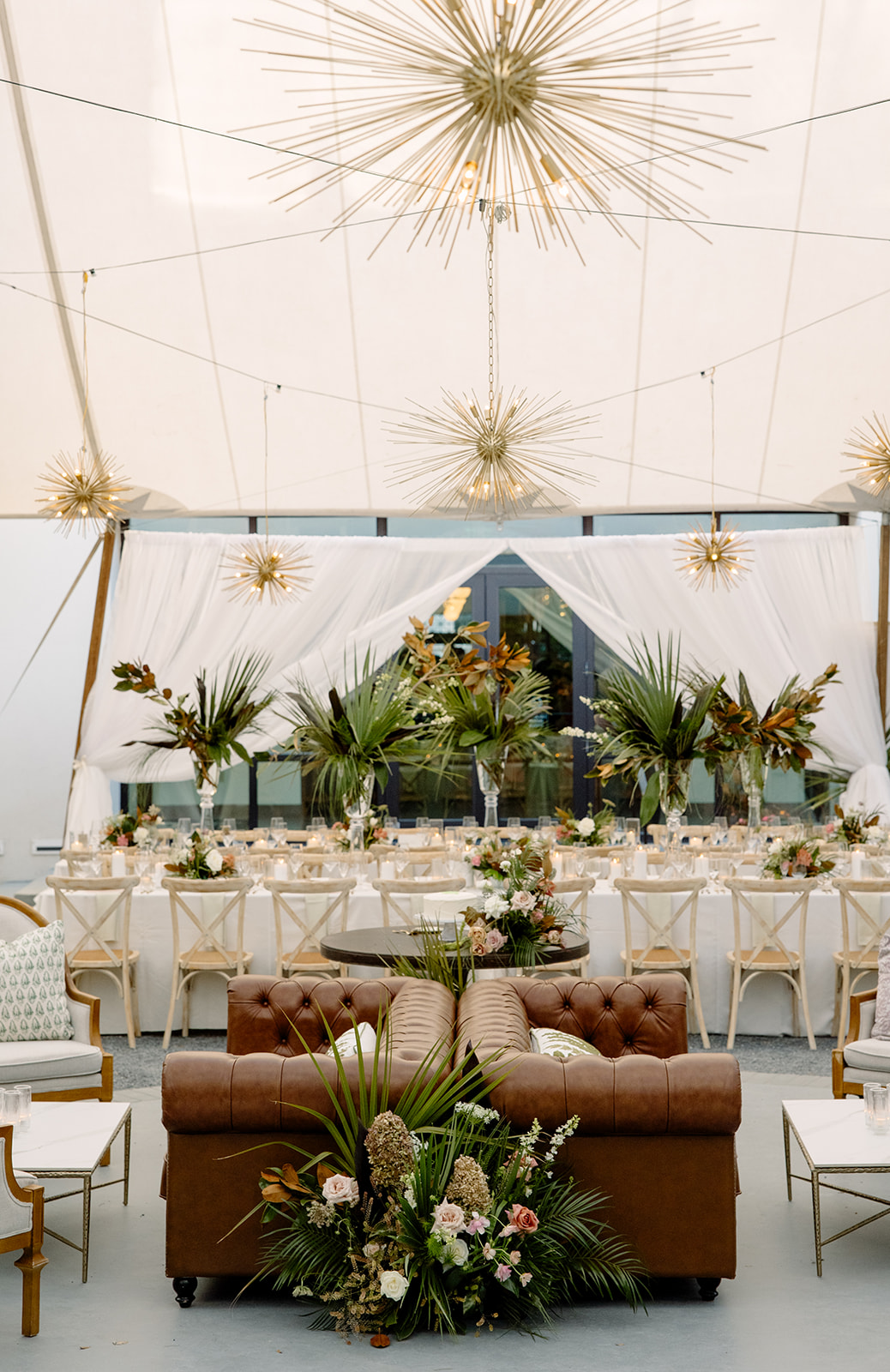 Elegant tent interior with draped fabric, greenery arrangements, and modern starburst chandeliers | Curated Events Elegant tent interior with draped fabric, greenery arrangements, and modern starburst chandeliers