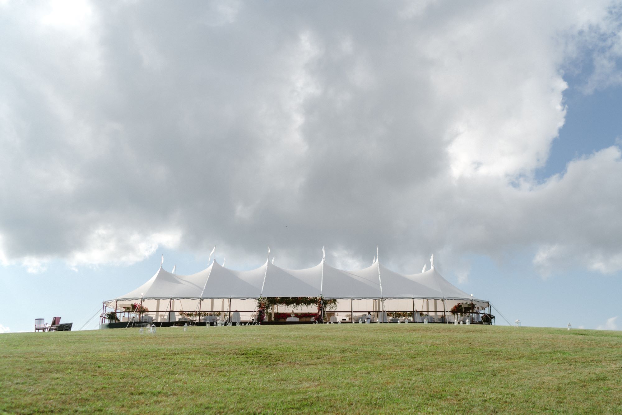 Long, stylish sailcloth tent on an open lawn under dramatic cloudy skies