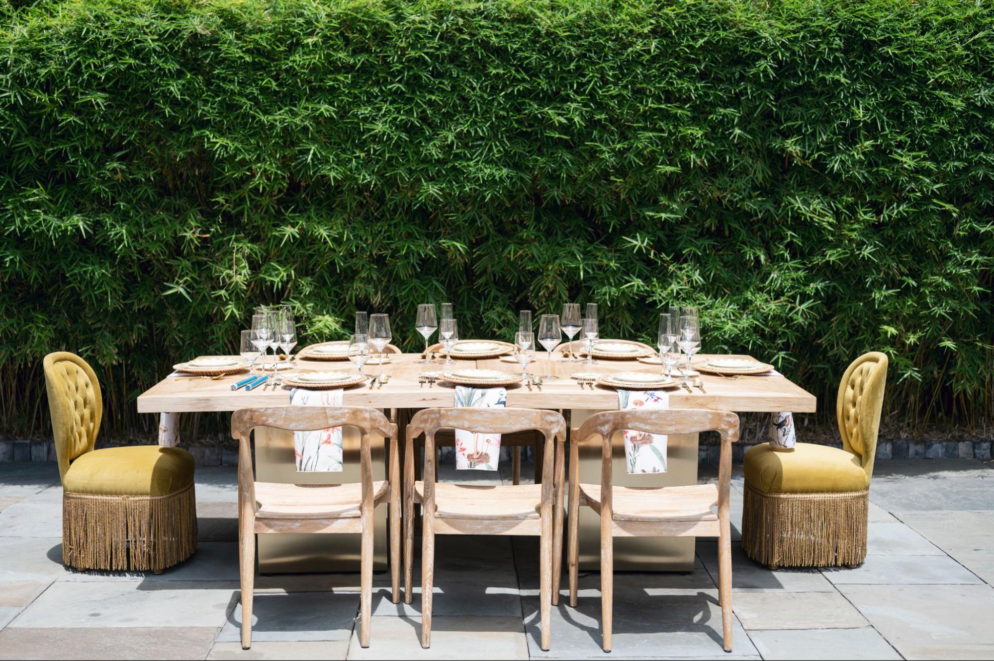 Outdoor corporate event dining setup with wooden table, formal place settings, and greenery backdrop.