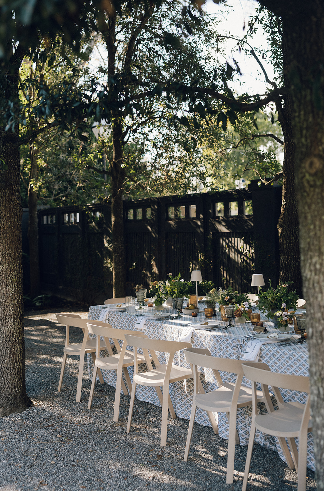Outdoor corporate dining setup under trees with patterned linens, formal place settings, and greenery centerpieces. | Curated Events Outdoor corporate dining setup under trees with patterned linens, formal place settings, and greenery centerpieces.