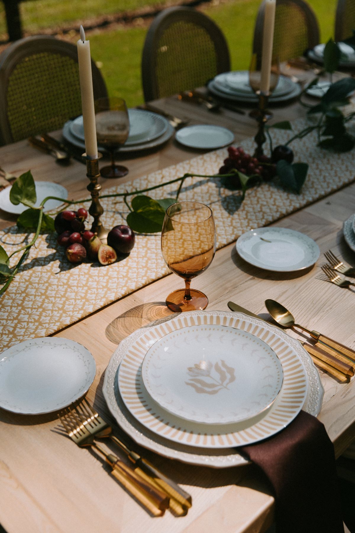 Corporate table styling with candles, fruit accents, and amber glassware on a wooden dining setup. | Curated Events Corporate event table setting with lighting and catering rentals, featuring decorative plates and glassware.