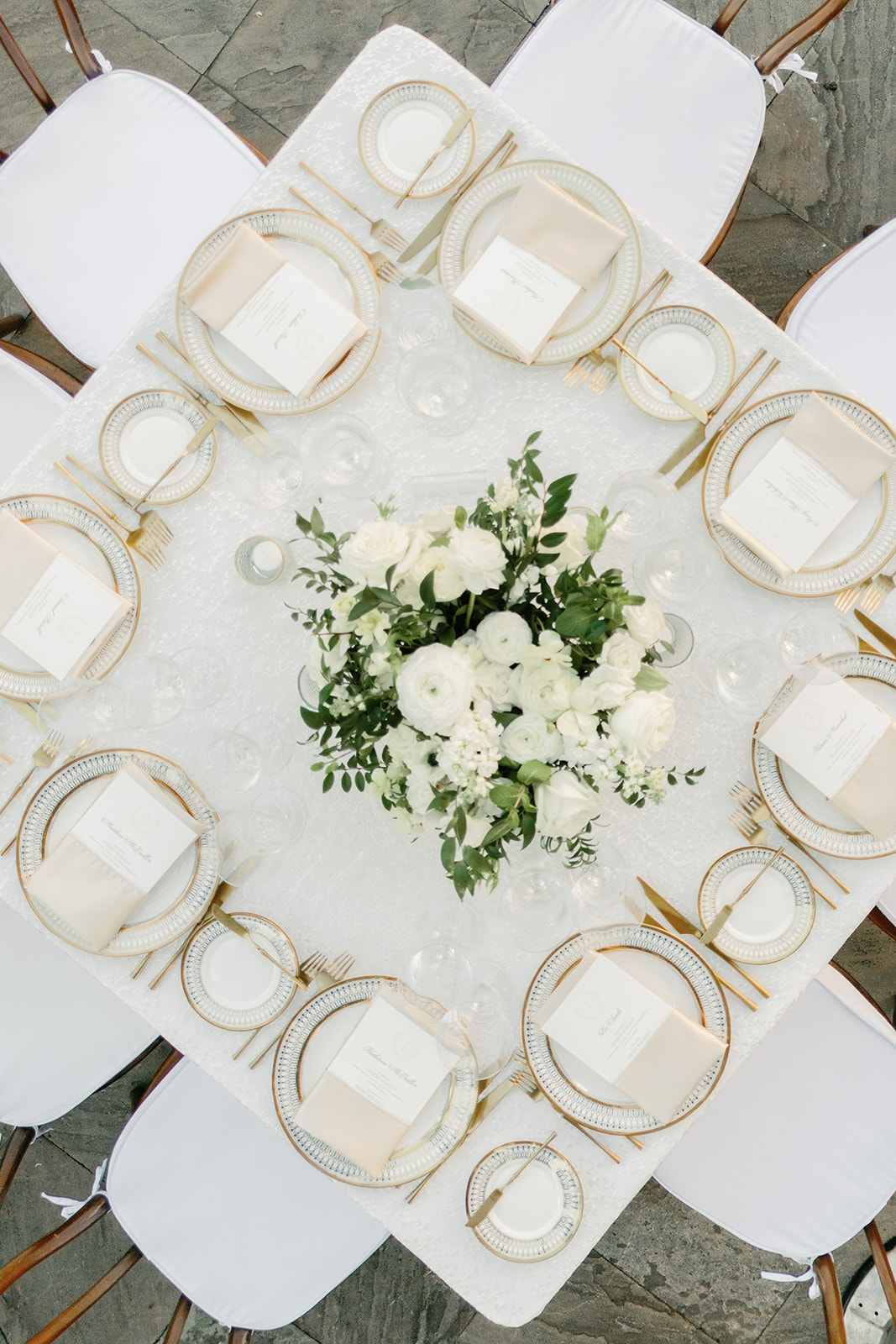 Overhead view of a white wedding reception table with gold flatware and floral centerpiece.