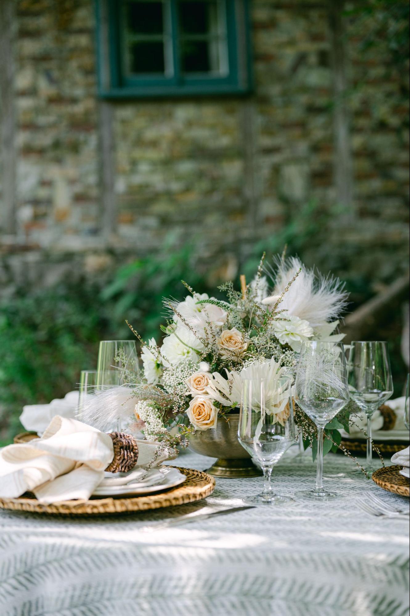 Elegant outdoor wedding table with neutral florals, glassware, and woven chargers.