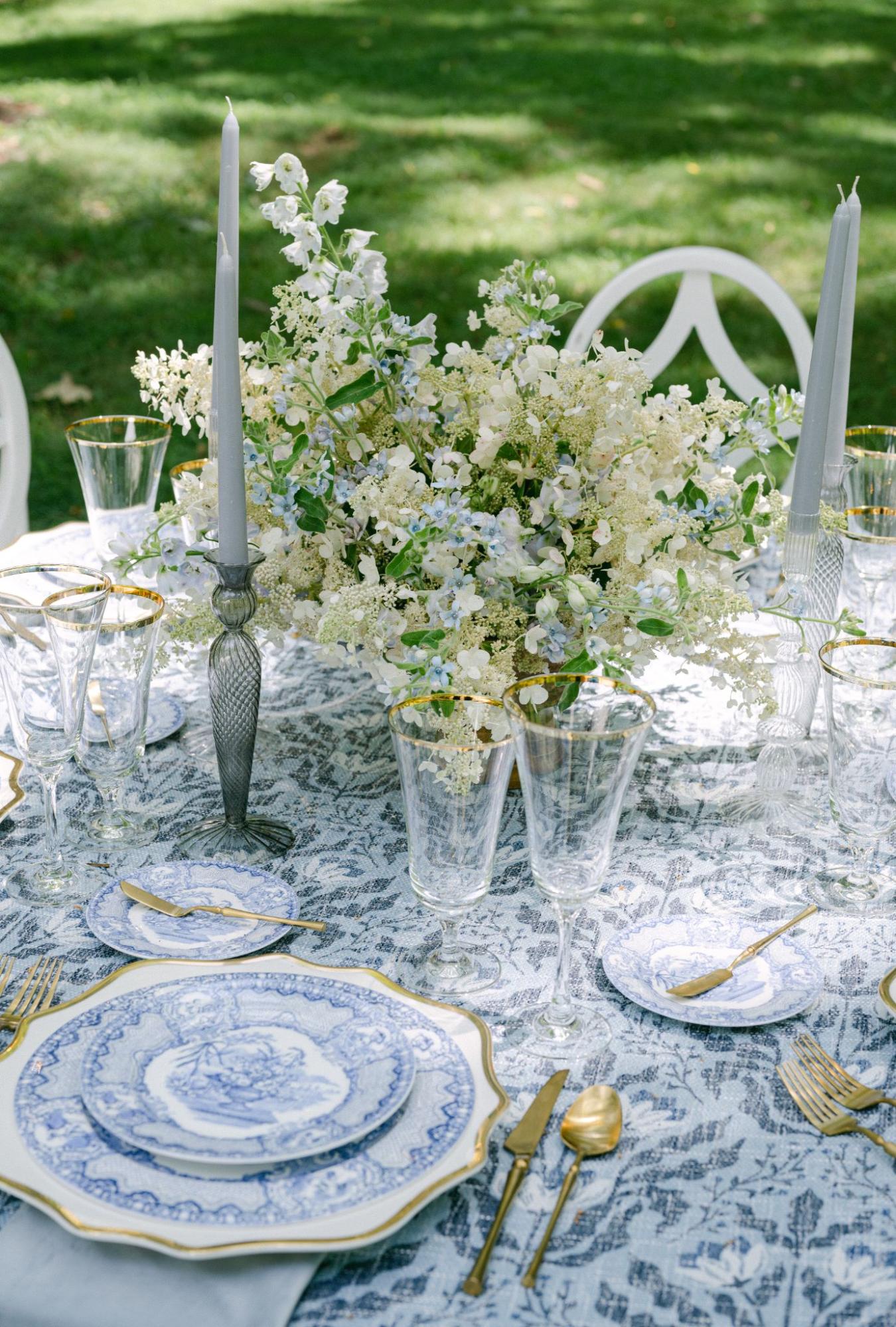 Blue-and-white patterned tablescape with white florals, glassware, and taper candles.