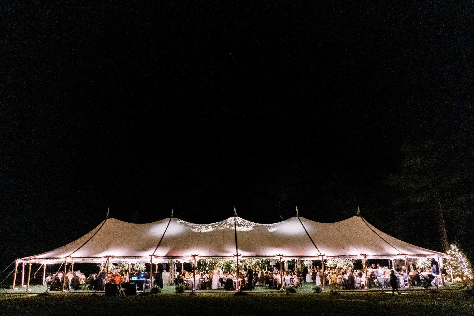 Large sailcloth tent glowing at night during an outdoor summer event.
