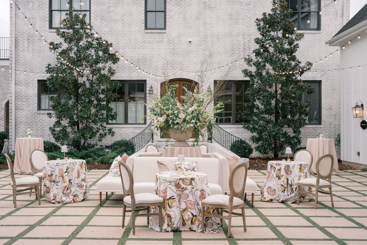 Courtyard lounge setup with patterned linens, cream seating, and floral centerpiece.