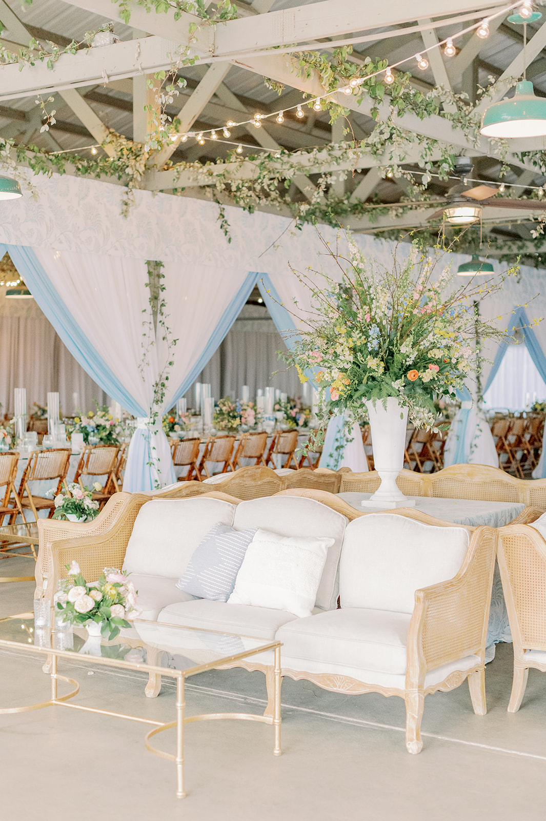 Light wood lounge seating with pastel florals and blue draping.