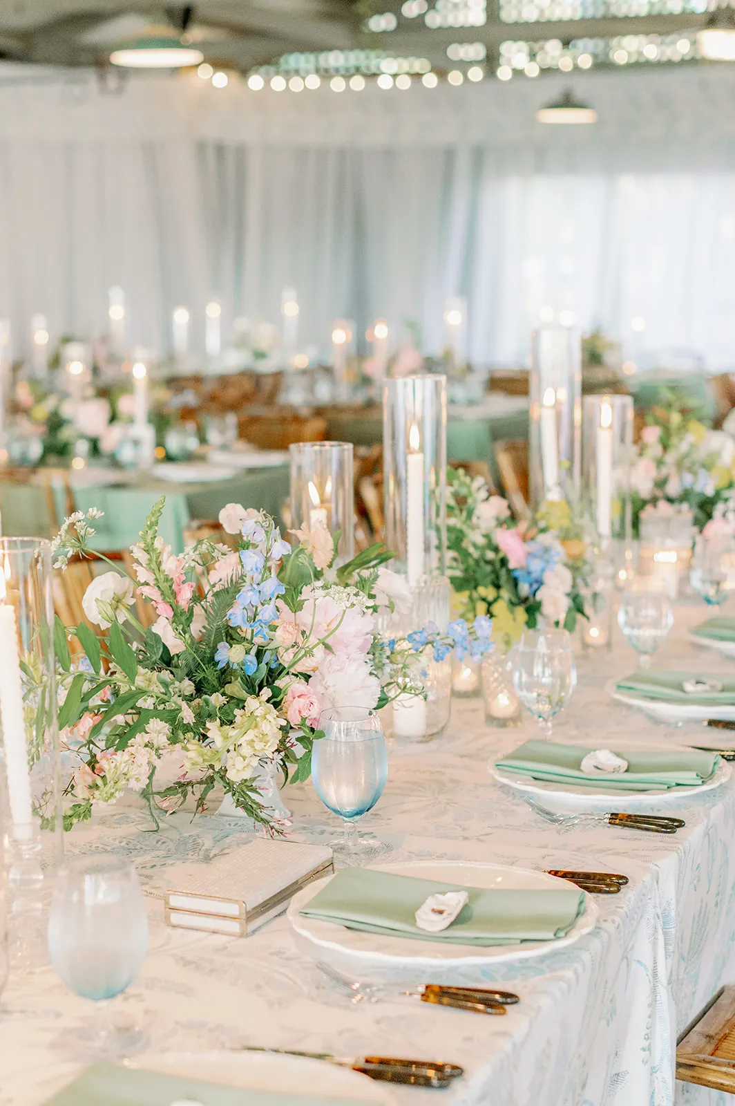 Long reception table with pastel flowers, blue goblets, and sage napkins | Curated Events Long reception table with pastel flowers, blue goblets, and sage napkins