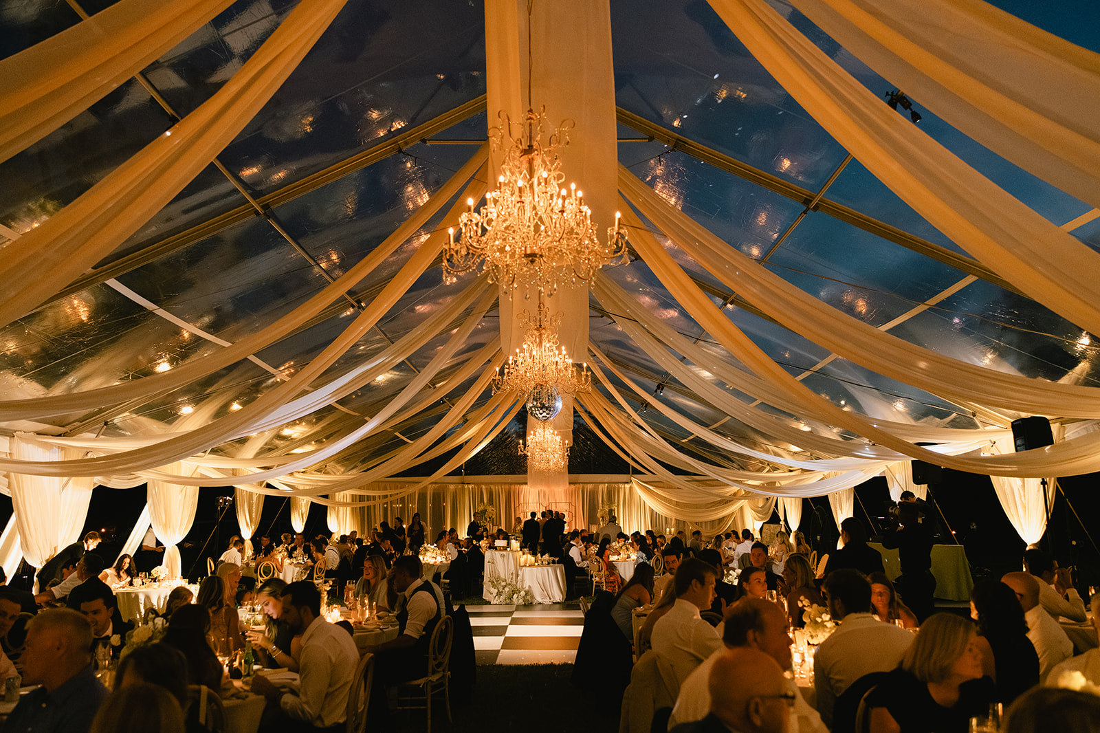 Evening tented event in Chesapeake with chandeliers, draped ceiling, and seated guests | Curated Events Evening tented event in Chesapeake with chandeliers, draped ceiling, and seated guests