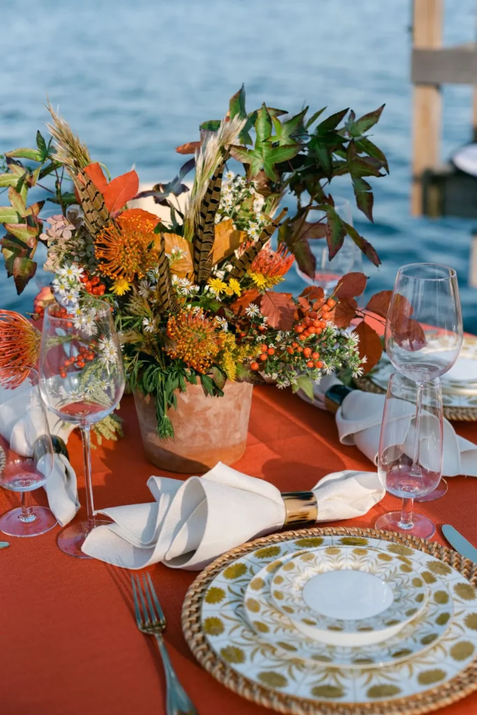 Rust-colored fall table linen with patterned china, gold napkin rings, and autumn flowers
