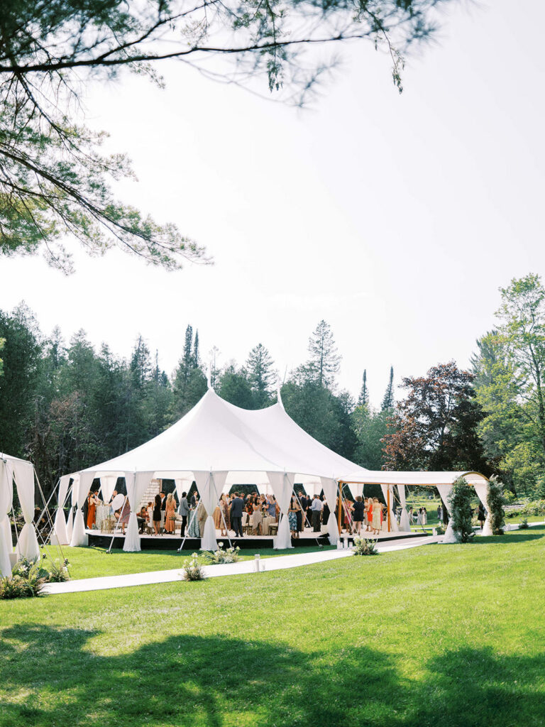 A large white tent set up for an outdoor event surrounded by trees and greenery.
