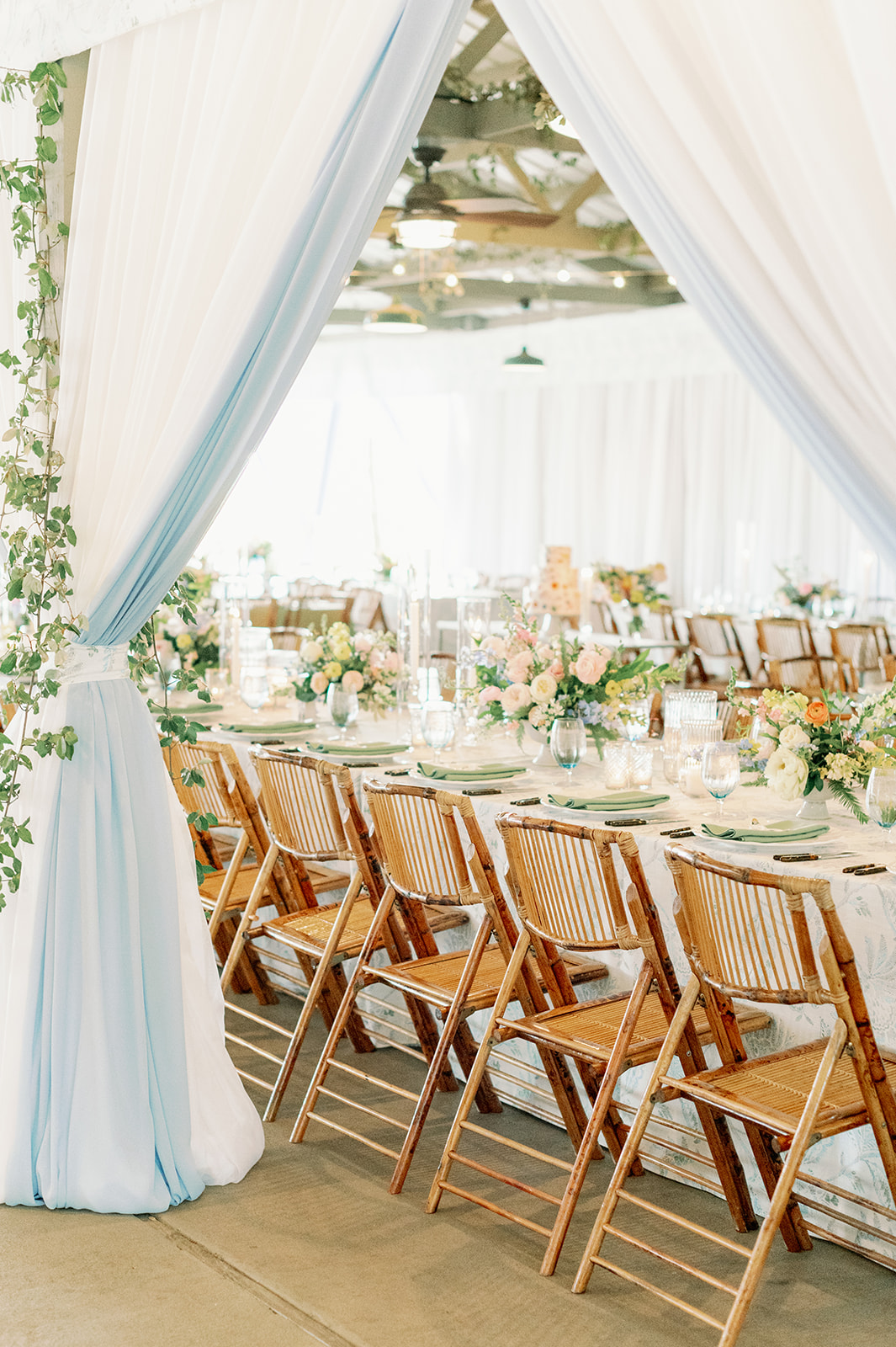 Bright summer tent rental setup with white draping, bamboo chairs, and elegant dining tables | Curated Events Bright summer tent rental setup with white draping, bamboo chairs, and elegant dining tables