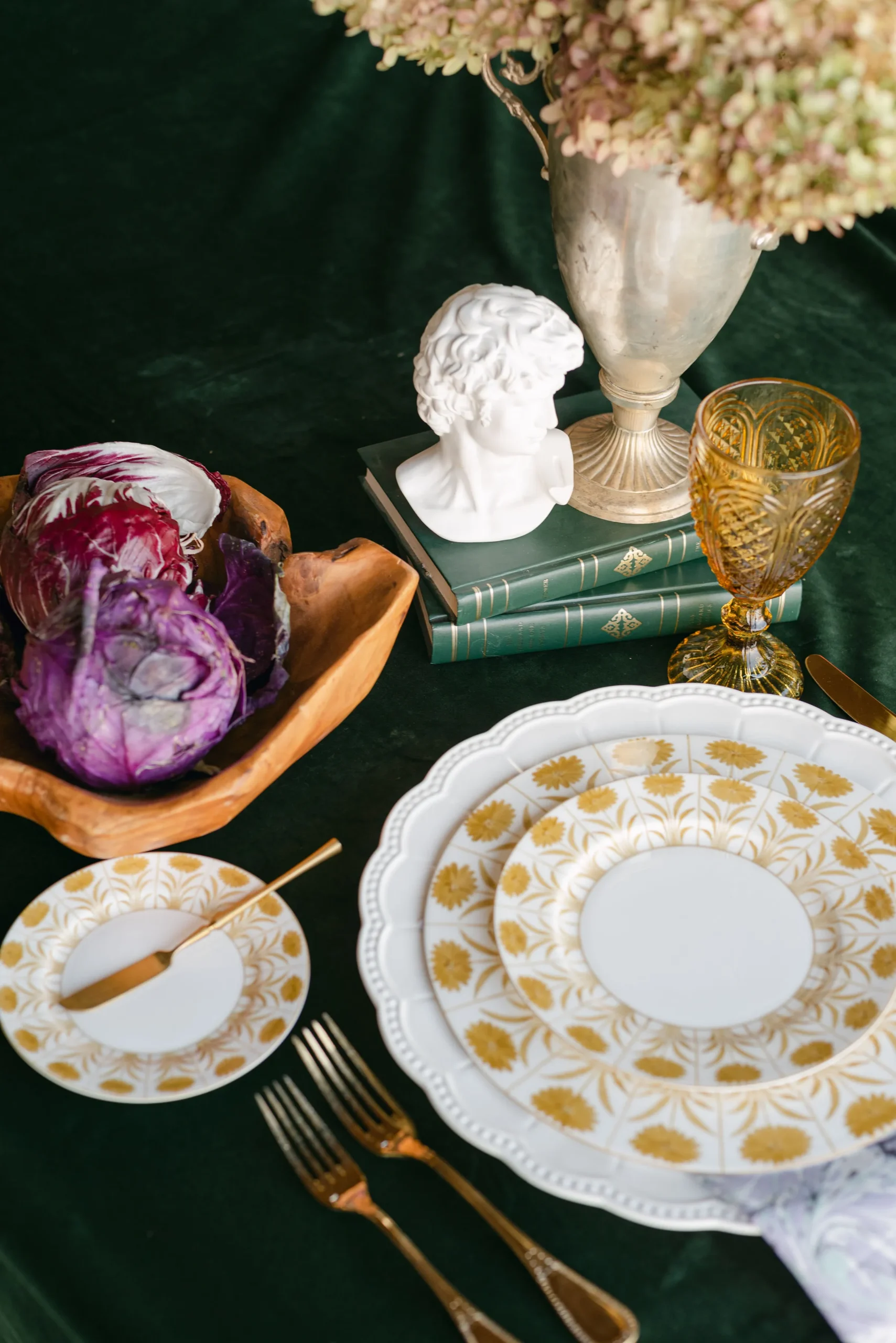 Gold-patterned china and amber glassware on a dark green tablecloth | Curated Events Gold-patterned china and amber glassware on a dark green tablecloth