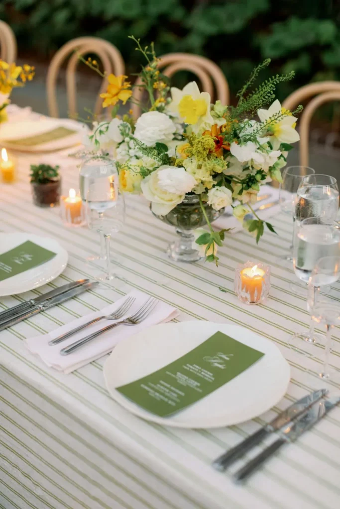 Wedding table with green striped linen, yellow and white flowers, candles, and glassware