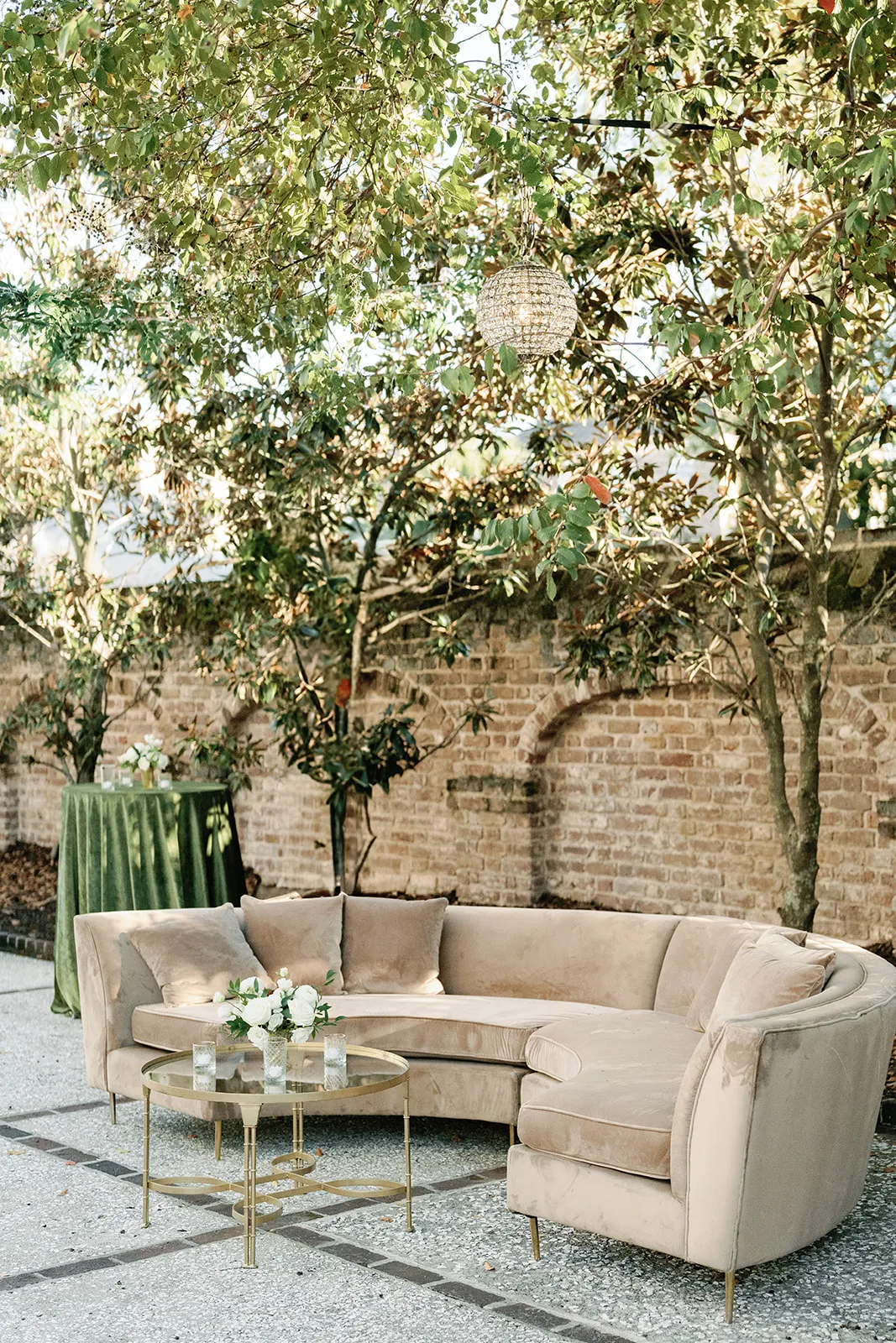 Curved beige sectional with a brass table in a brick courtyard