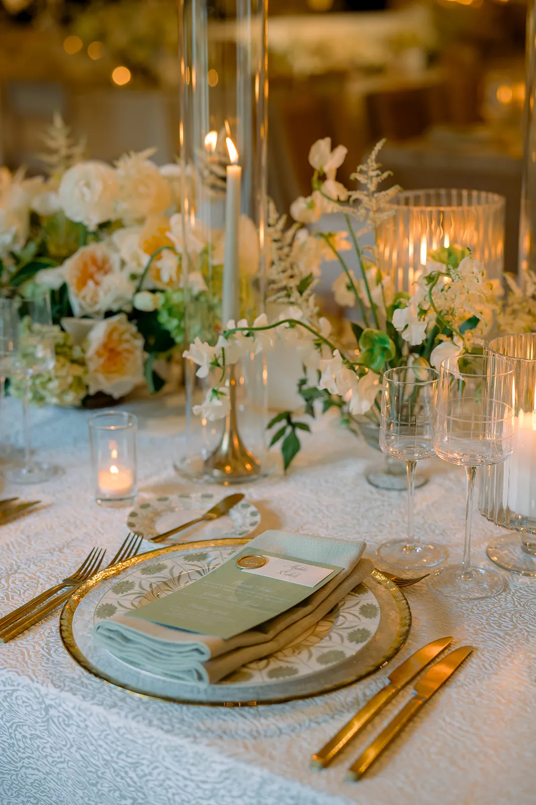 Candlelit place setting with floral china, sage napkin, and gold flatware