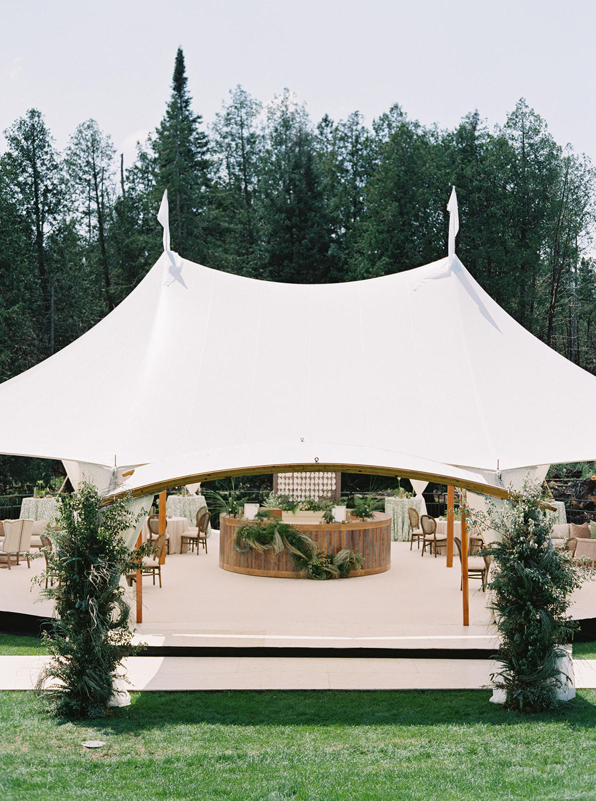 Elegant white tent set up for an outdoor event, surrounded by greenery.