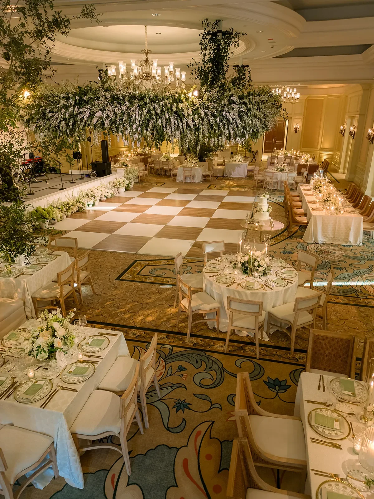 Ballroom wedding reception with a checkered dance floor, candlelit tables, and hanging white flowers