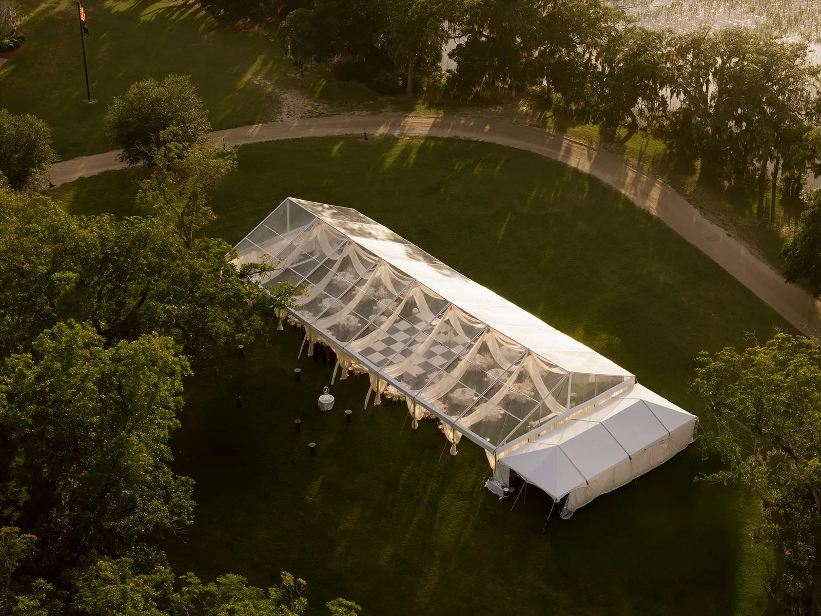 Aerial view of a clear-top wedding tent with ceiling draping and a checkered dance floor