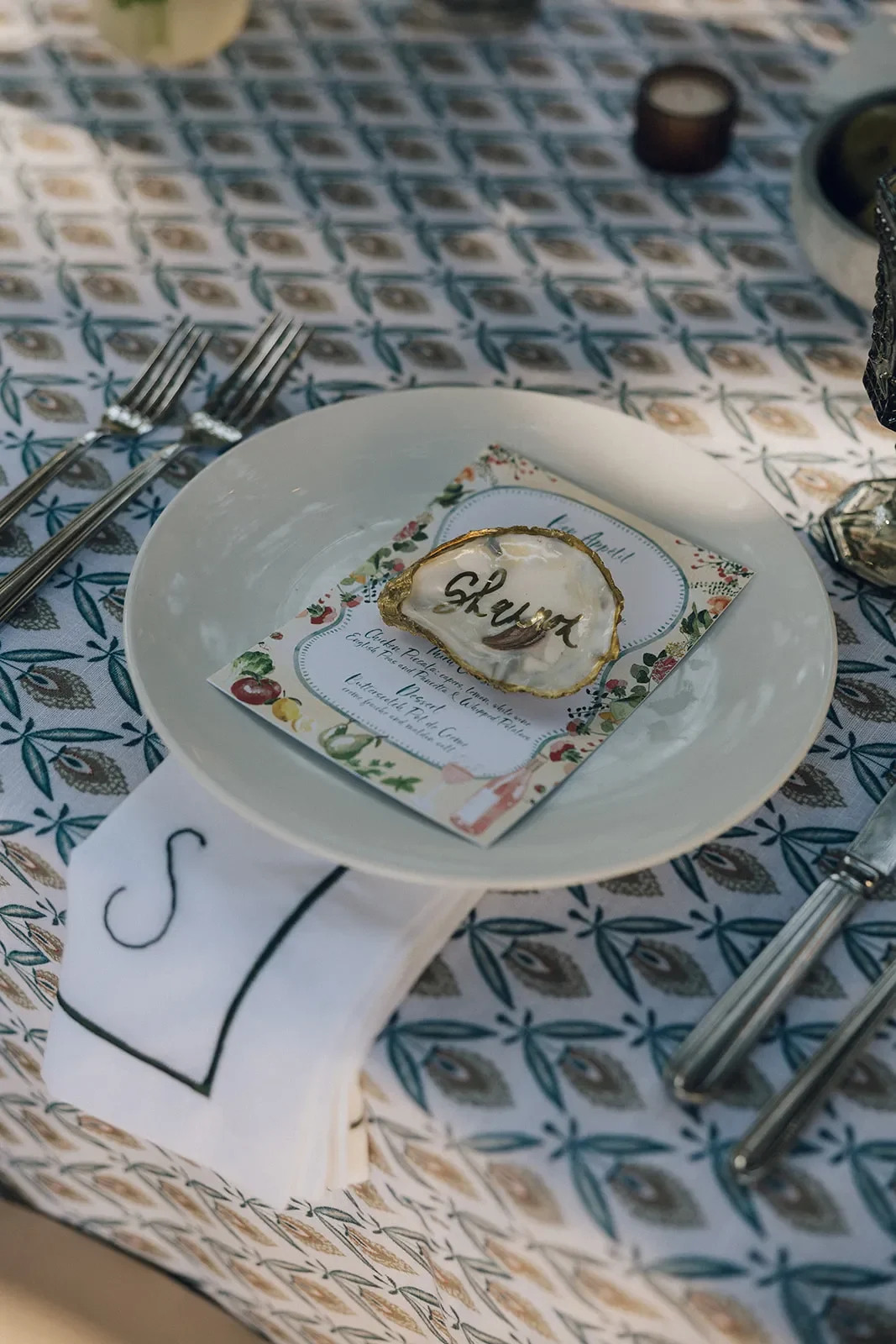 Wedding place setting with a personalized shell place card on blue patterned linen