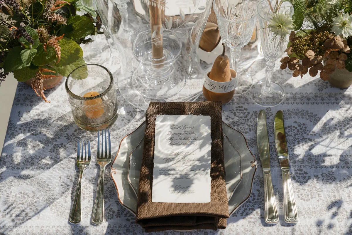 Layered place setting with clear glassware, silver flatware and a textured napkin on patterned linen