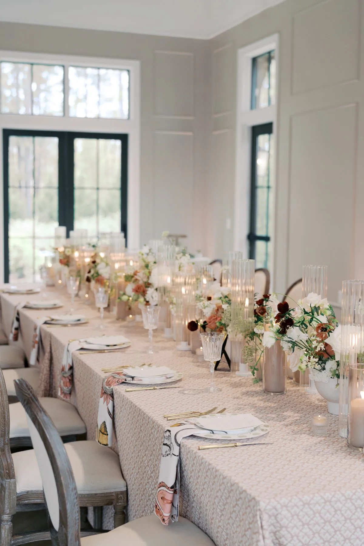 Long formal dining table with neutral linens, candles, florals, and upholstered chairs