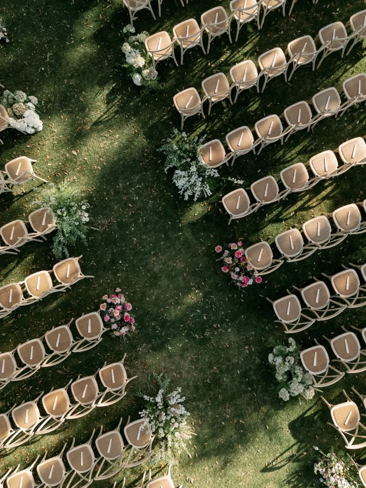 Overhead view of cane-back wedding chairs arranged around a flower-lined outdoor ceremony aisle