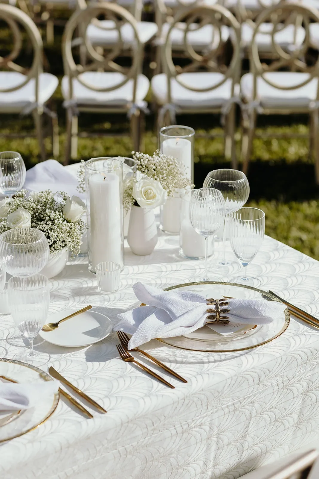White textured table linen with gold flatware, ribbed glassware, candles, and white roses